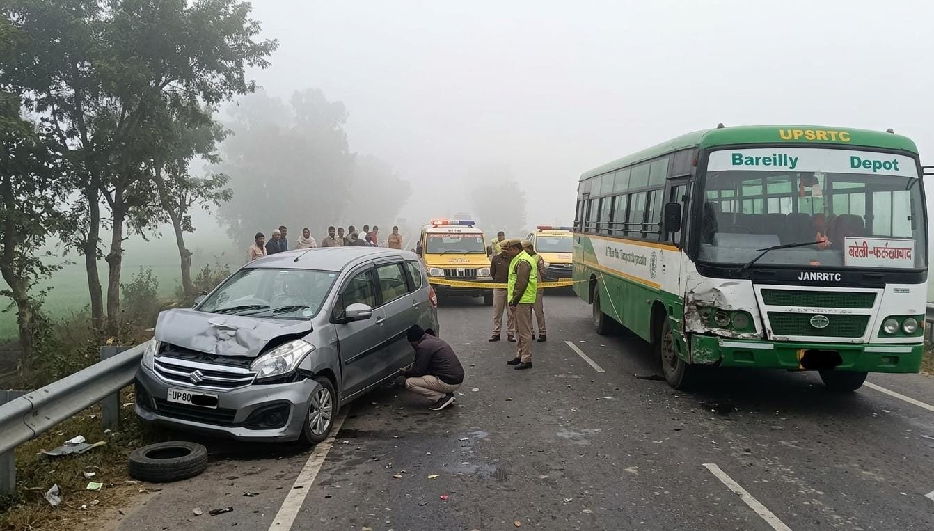 कोहरे के कारण बीसलपुर-बेबर राष्ट्रीय राजमार्ग पर एक क्षतिग्रस्त चांदी के रंग की अर्टिगा कार और यूपी रोडवेज की बस (बरेली डिपो) के बीच टक्कर का दृश्य, साथ ही मौके पर मौजूद पुलिस और बचाव दल।